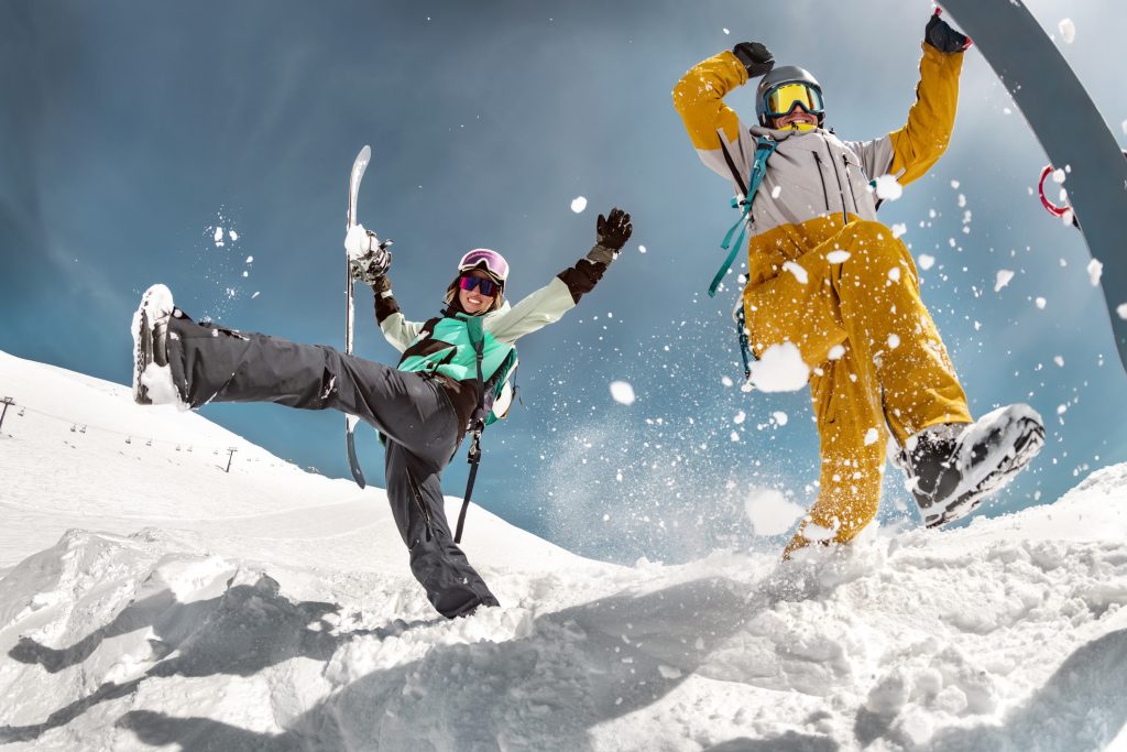 Happy couple of snowboarders are having fun and jumps with snowboards in hands. Winter holidays at ski resort