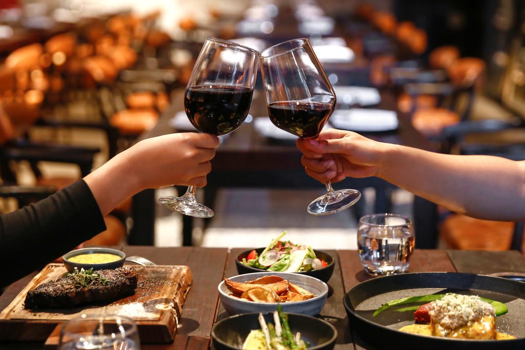 Close up two people holding wine glasses, toasting on their dinner table