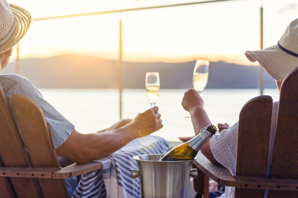 Couple relaxing and drinking champagne on deck chairs on the waterfront. They are toasting with the champagne.